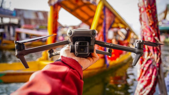 A hand holds a drone against a vibrant backdrop of colorful boats, showcasing travel and technology.