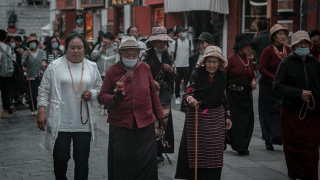 A group walks through a bustling street in Tibet, showcasing traditional attire and vibrant local culture.