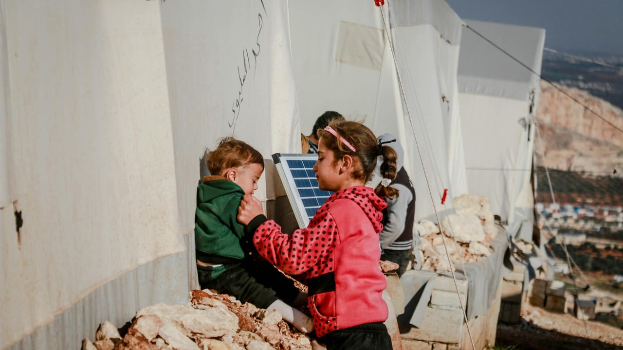 Tender moment between siblings at refugee camp in Idlib, Syria. Outdoor setting with tents.