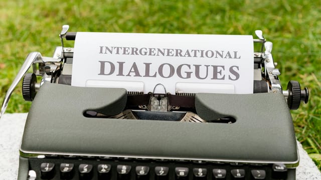 Close-up of a vintage typewriter outdoors with paper reading 'Intergenerational Dialogues'.