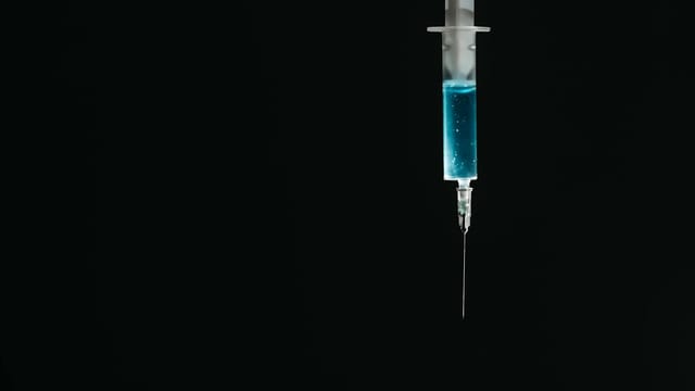 A detailed image of a syringe filled with blue liquid against a black backdrop, symbolizing medical themes.