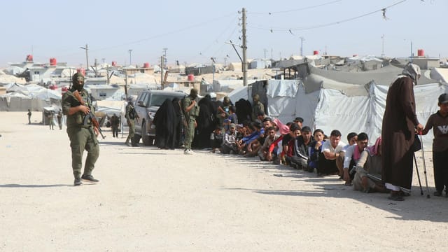 Refugees in al-Hol camp, Syria, guarded by soldiers, highlighting humanitarian crisis.
