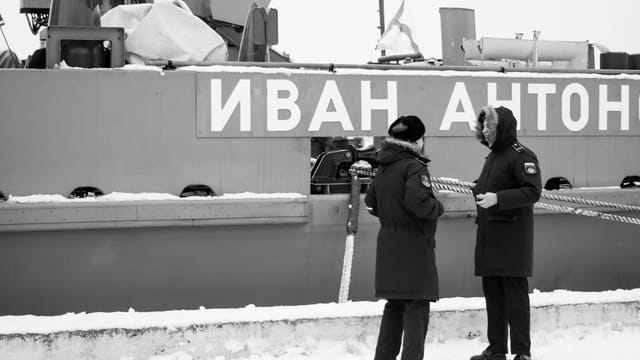 Russian naval officers converse by the warship Ivan Ant in winter.