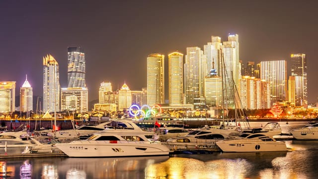 Qingdao's marina with motor yachts and glowing skyscrapers at night, showcasing its vibrant cityscape.