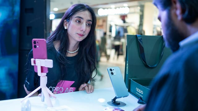 Woman at smartphone demo counter engages with salesperson in Islamabad retail setting.