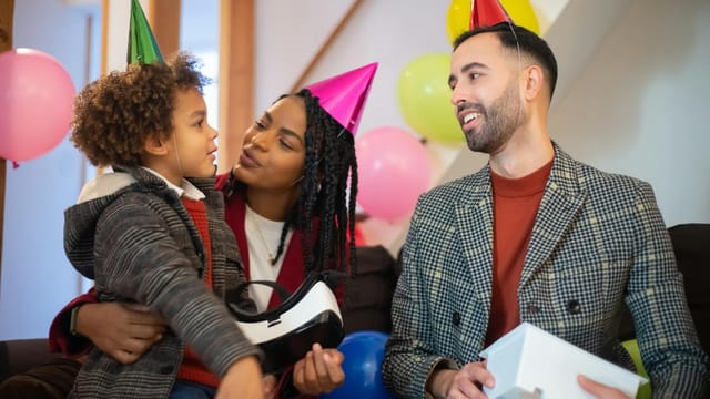 A diverse family celebrates a birthday with party hats, balloons, and a VR gift, spreading love and joy.