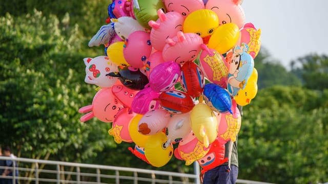Vibrant cartoon character balloons being sold outdoors on a sunny day in a park.