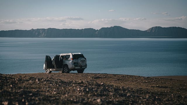 White SUV parked by a scenic lake in Tibet, surrounded by mountains and clear skies.