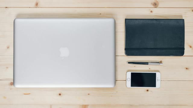 A clean, organized desk featuring a laptop, smartphone, notebook, and pen, ideal for productivity.