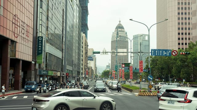 View of a busy street in Taipei featuring traffic and modern high-rise buildings. Captured during the day.