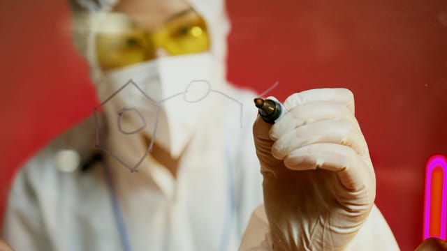 Scientist writes chemical formula on transparent surface in lab. Focus on hand and pen.