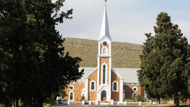 A beautiful church with a clock tower amidst lush trees on a sunny day in Joubertina, South Africa.