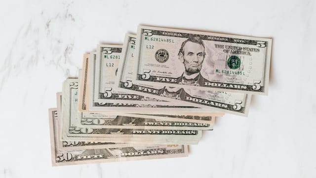Stack of various US dollar bills on a clean marble surface, emphasizing finance and currency.