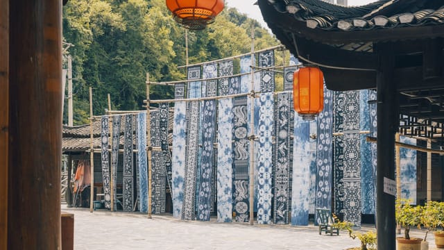 Colorful blue and white textiles drying outdoors in a traditional Chinese market setting under red lanterns.