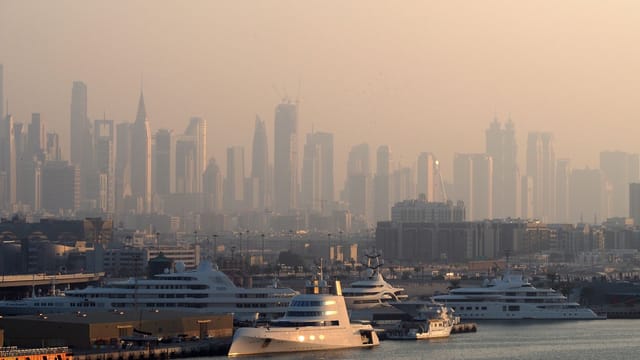 Dubai Marina with luxury yachts against a skyline of iconic skyscrapers in the morning light.