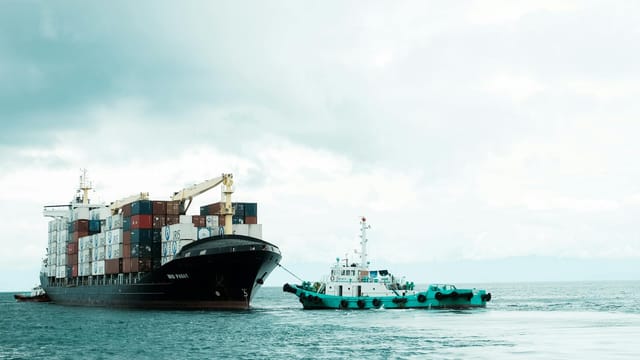 A container ship and tugboat navigate the waters of Davao City, Philippines, under a cloudy sky.