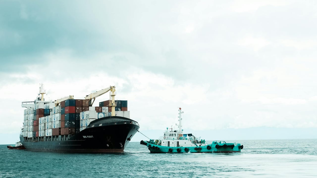 A container ship and tugboat navigate the waters of Davao City, Philippines, under a cloudy sky.