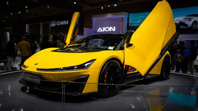 Yellow sports car with gullwing doors showcased at an indoor auto exhibition.