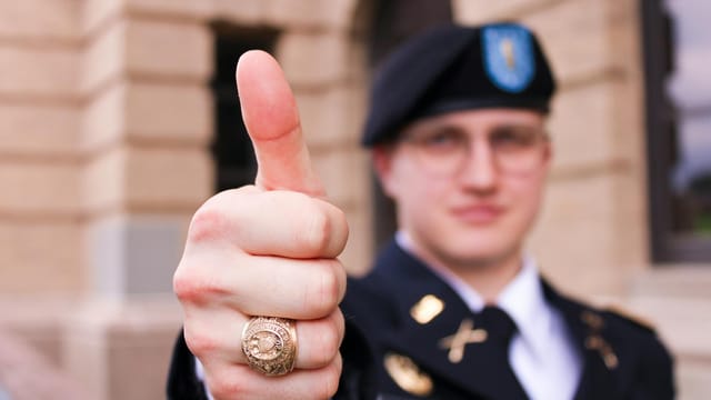 Close-up of military officer wearing uniform giving thumbs up gesture, ring visible.