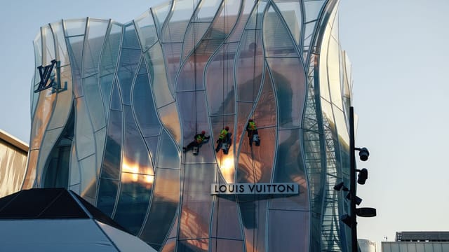 Workers cleaning the unique glass facade of a modern Louis Vuitton building.