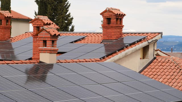 Illustrative image: Solar panels on tiled roofs of houses with chimneys, capturing clean energy.
