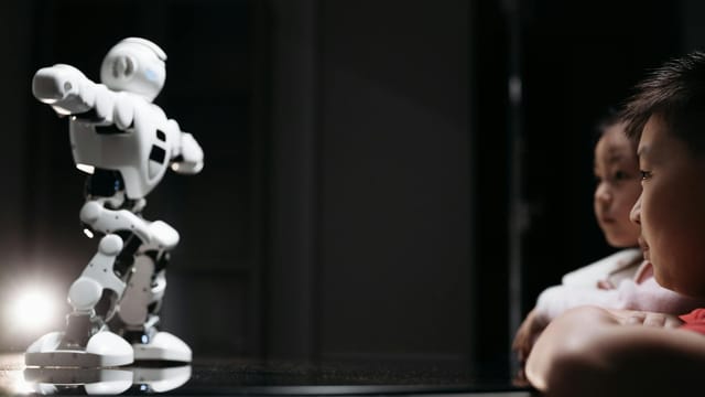 Children watching a humanoid robot toy on a reflective surface, showcasing innovation and curiosity.