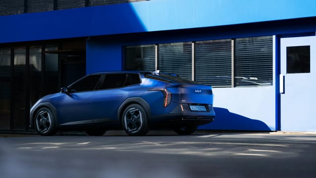 A modern blue electric vehicle parked outside a contemporary building on a sunny day.