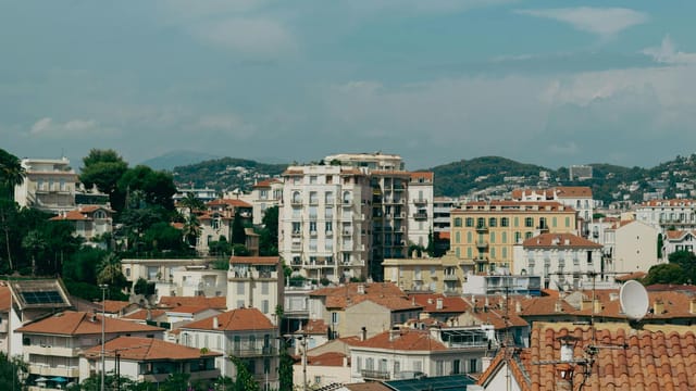 Explore the charming architecture of Cannes, France, set against lush hills and a bright sky.