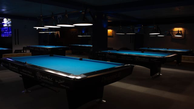 A row of empty billiard tables in a dimly lit gaming lounge.