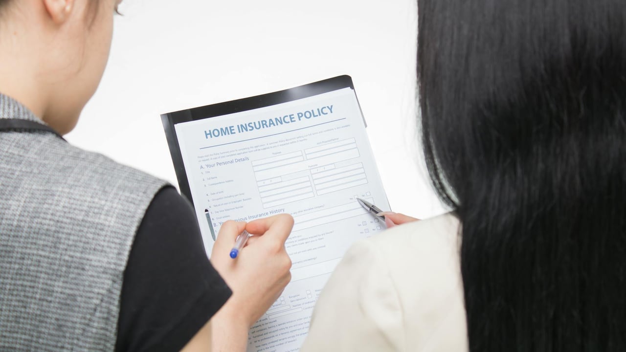 Two women examining home insurance policy form, focused on details.