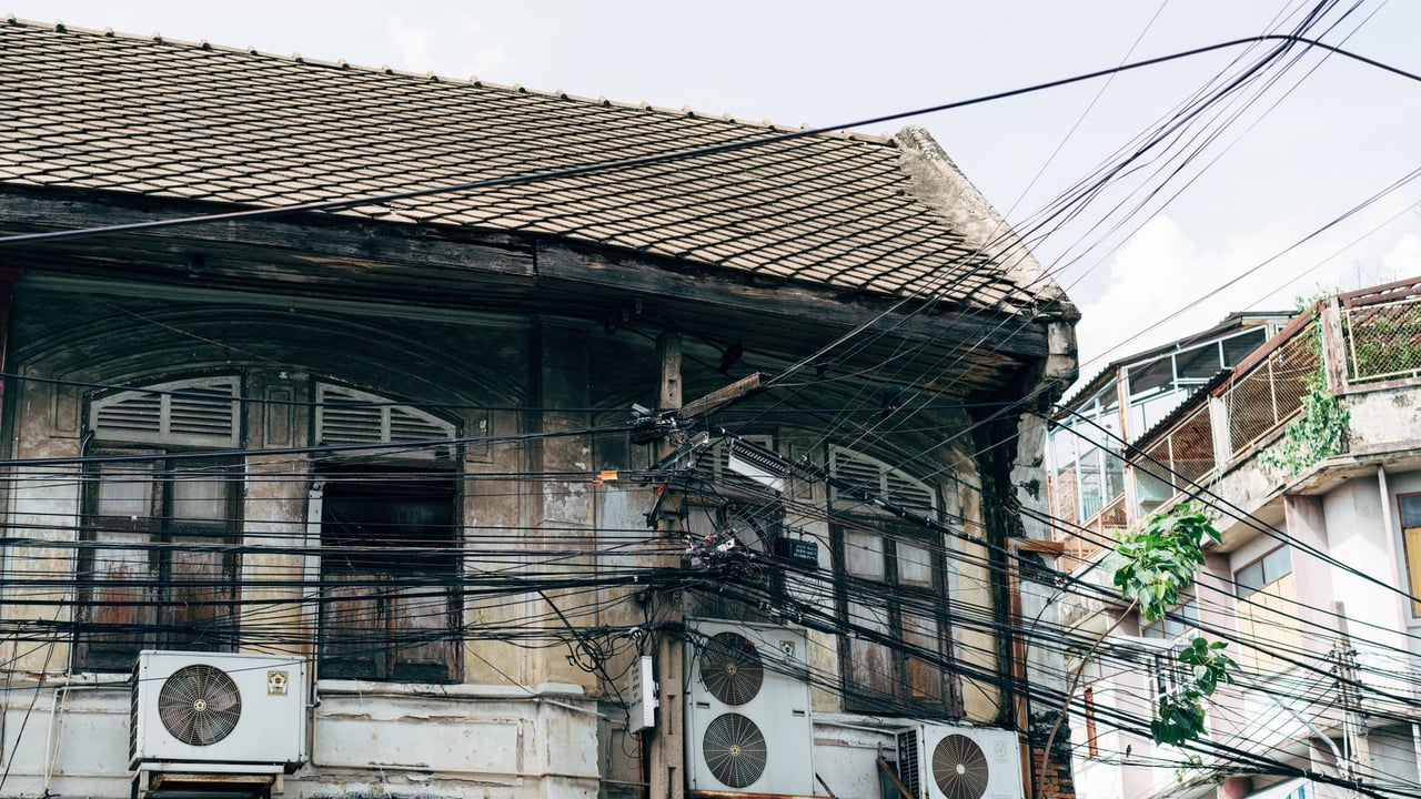 A weathered building with roof tiles and electric wires in an urban area, showcasing vintage architecture.