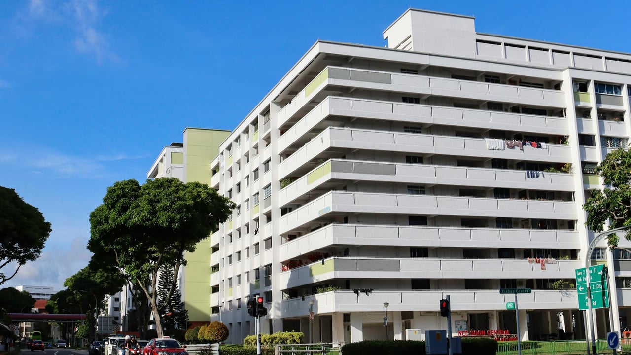 A busy urban street intersection with modern high-rise residential buildings under a clear blue sky.