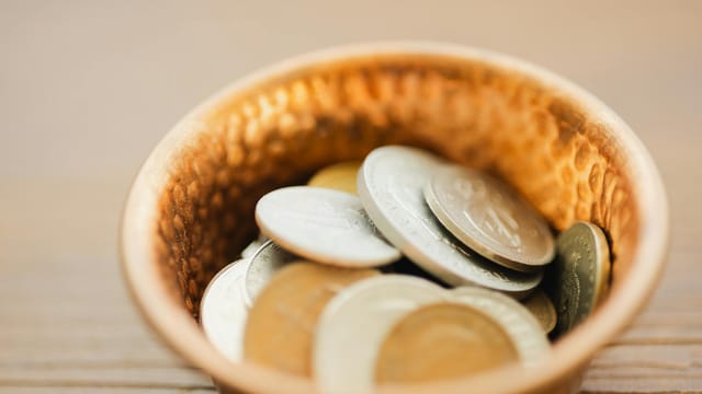 A detailed view of various coins in a vintage textured metal bowl, showcasing texture and currency.