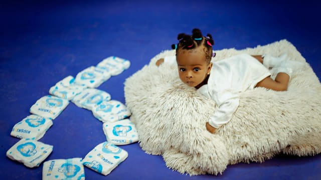 Cute baby lying on a soft rug with diapers arranged in a heart shape.