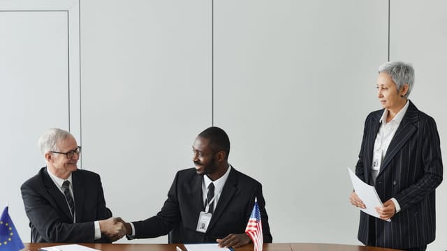 Multinational business meeting with agreement signing, featuring diverse professionals and flags.