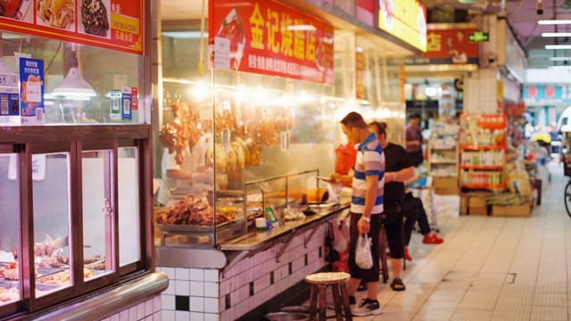 Man browsing food options at busy indoor street market stall.