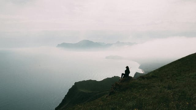 A woman sits on a cliff in Коктебель, enjoying the serene view of the misty coastline.