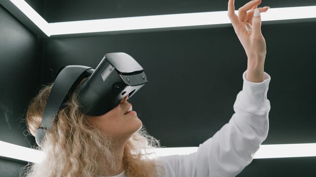 A woman wearing a headset engages with virtual reality, reaching out her hand.