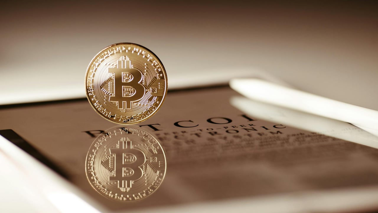 Close-up of a gold Bitcoin reflecting on a digital tablet screen, showcasing cryptocurrency concepts.