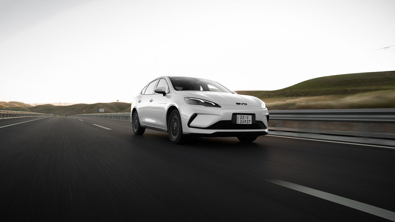 A modern white car drives on an open highway at dawn, highlighting sleek design and open road adventure.