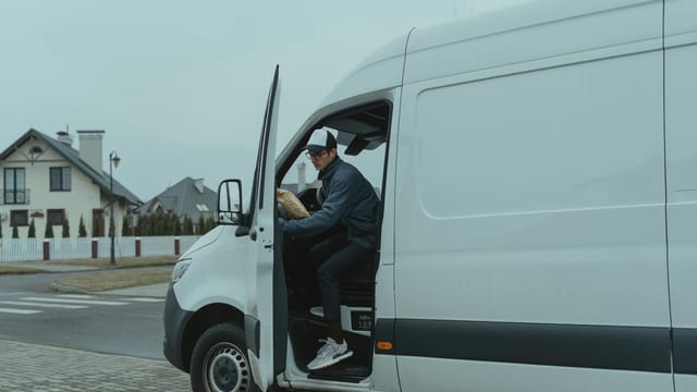 Courier delivering a package from a van in suburban neighborhood, showcasing logistics and last-mile delivery services.