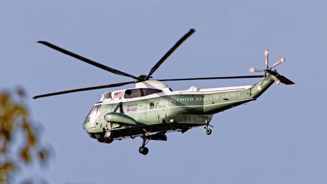 A SH-3 Sea King helicopter with USA markings flying outdoors on a clear day.