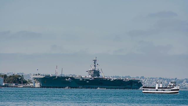 USS Carl Vinson aircraft carrier docked in San Diego harbor with a ferry in view.