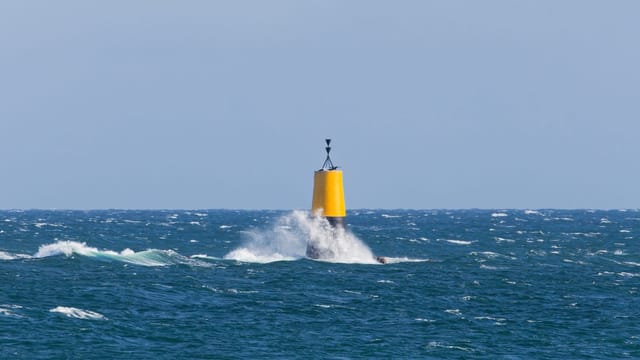 A bright yellow buoy amidst crashing waves in the Atlantic Ocean off the coast of Brittany, France.