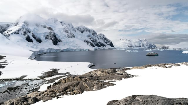 Scenic Antarctic view with icy mountains, calm waters, and a solitary boat.