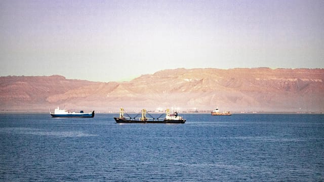 Serene view of cargo ships navigating the Suez Canal with mountains in the background.