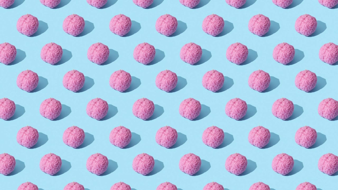 Creative composition of pink brain models in a repeating pattern on a light blue surface, showcasing abstract thinking.