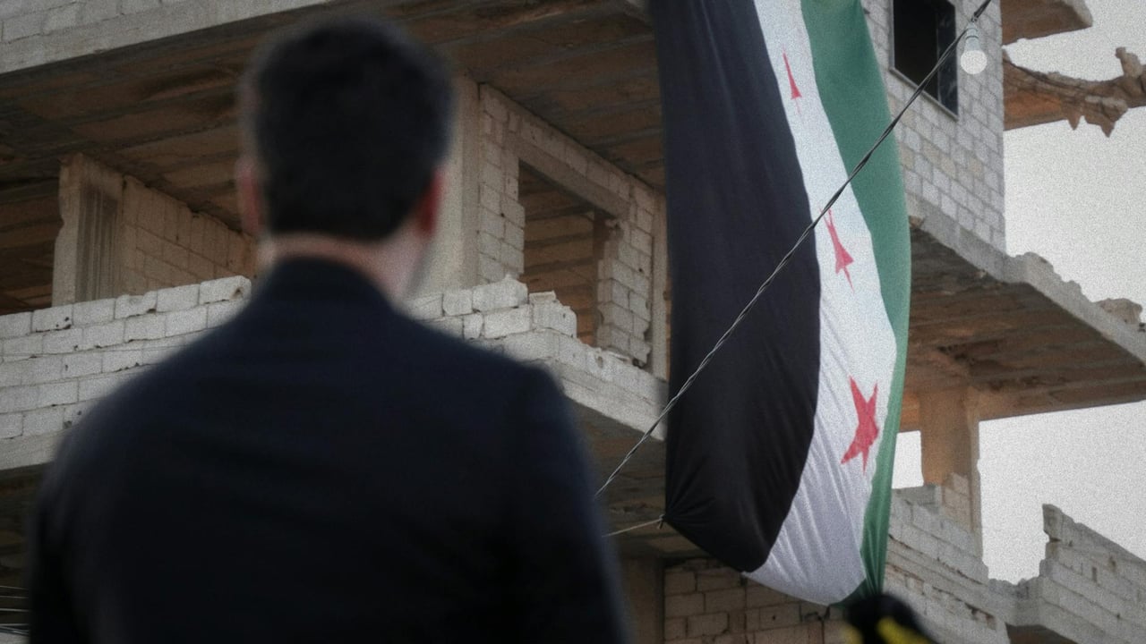 A man observes a Syrian flag draped over a war-torn building in Damascus, Syria.