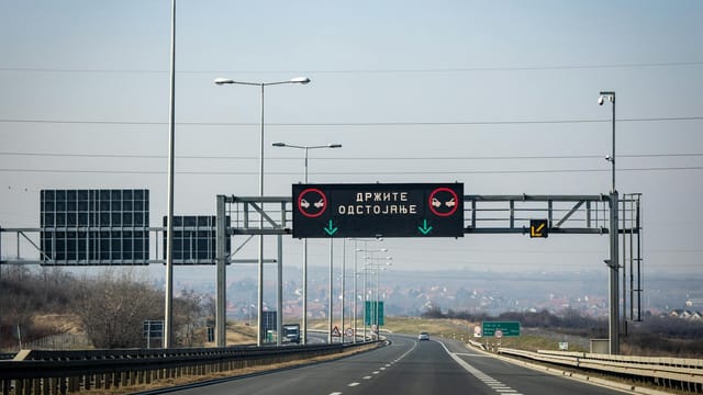 View of a highway with a digital traffic sign under a clear blue sky.