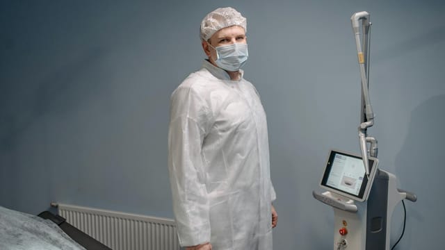 Doctor in protective gear standing beside medical equipment in a sterile room.